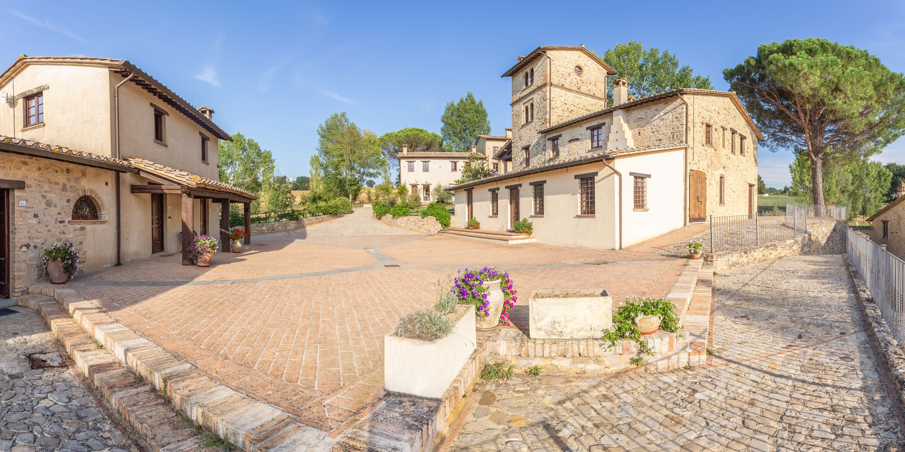 Un patio empedrado con edificios históricos, muros de piedra y plantas en macetas.
