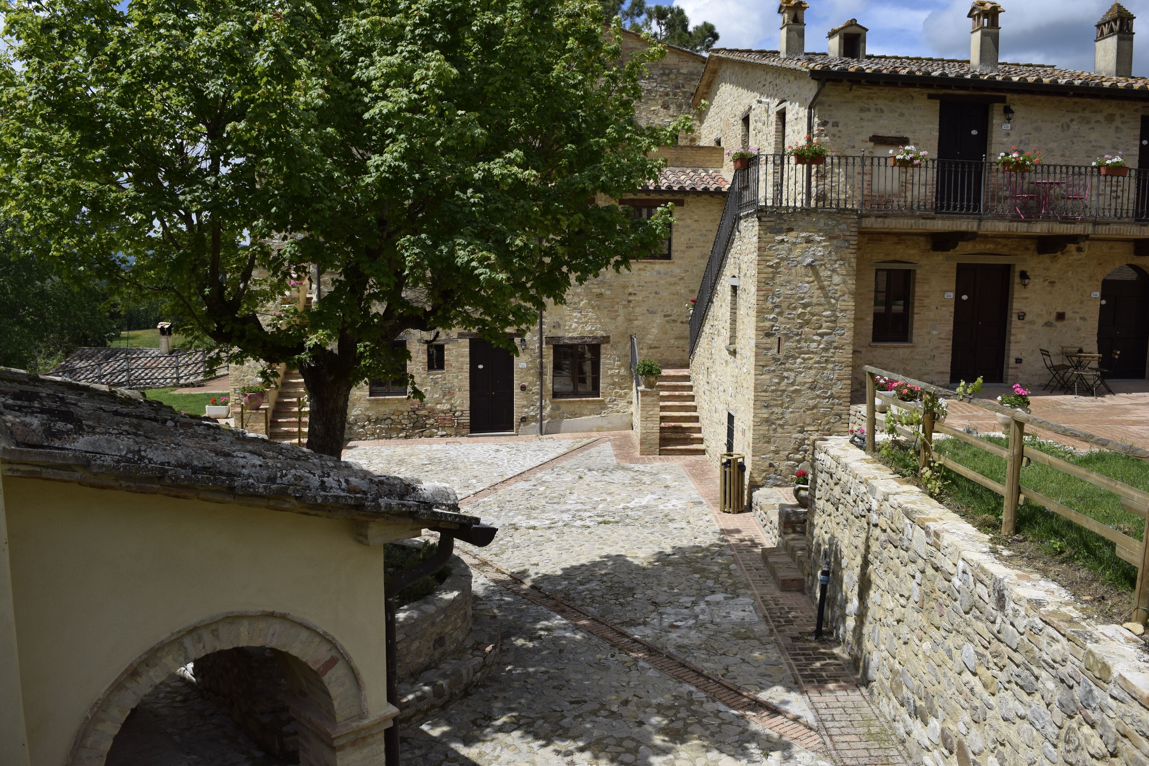 A stone building with a courtyard, a tree, and a staircase leading to an upper level.