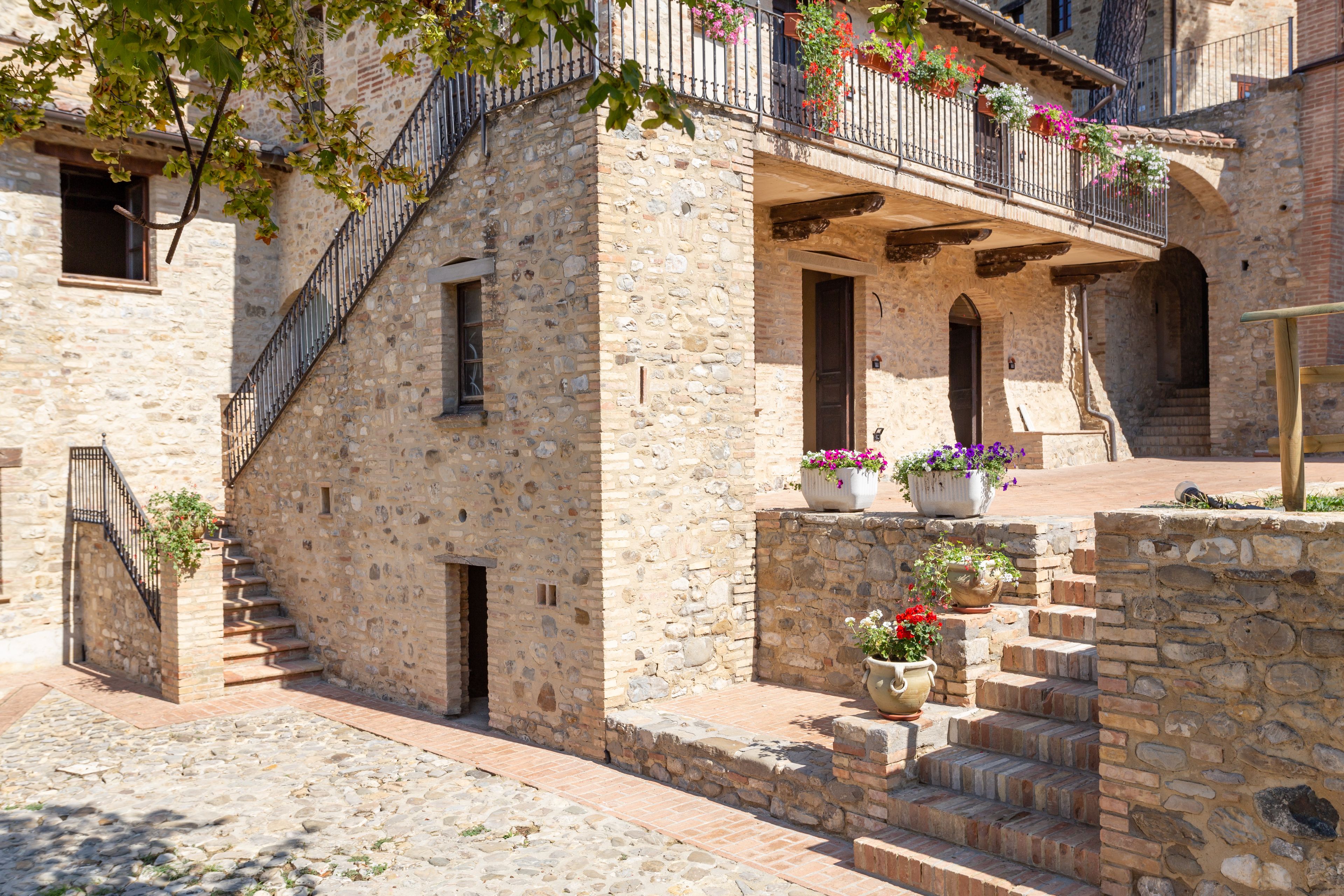 Un edificio de piedra con una escalera que conduce a un balcón decorado con plantas en macetas.