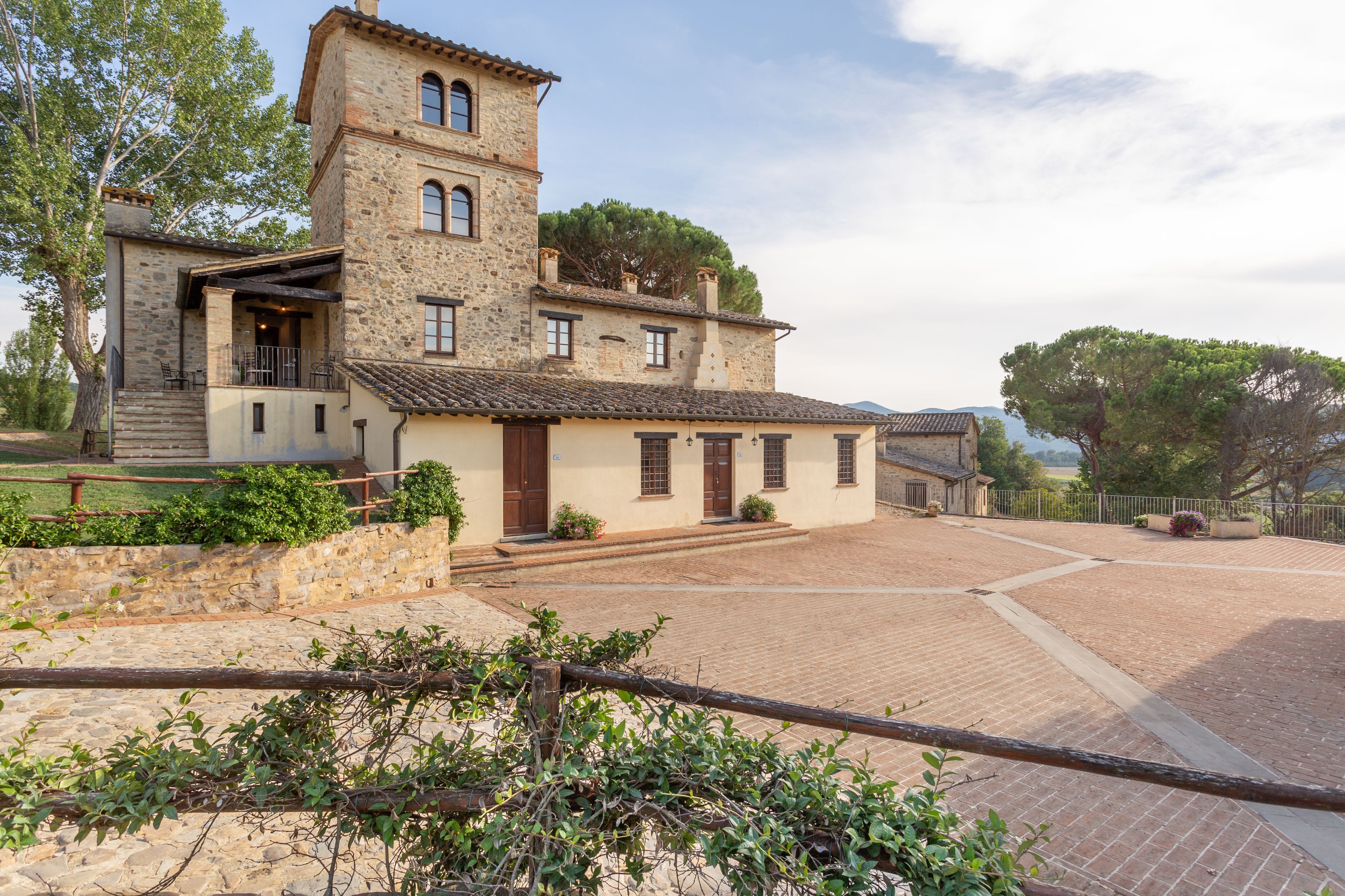 Un bâtiment en pierre doté d’une tour, d’une cour pavée et entouré de verdure.