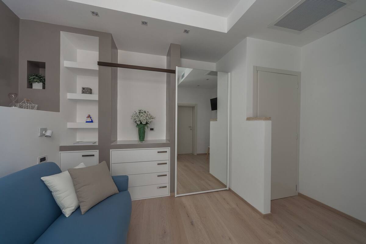 A modern, well-lit room with a blue sofa, a white dresser, and a mirror.