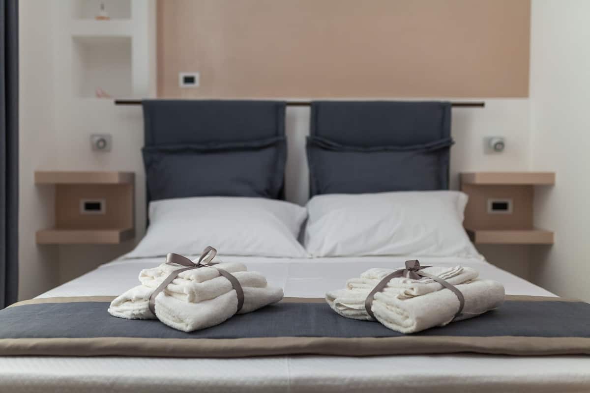 A neatly made bed with two towels tied with a ribbon, a headboard, and bedside tables with small shelves.