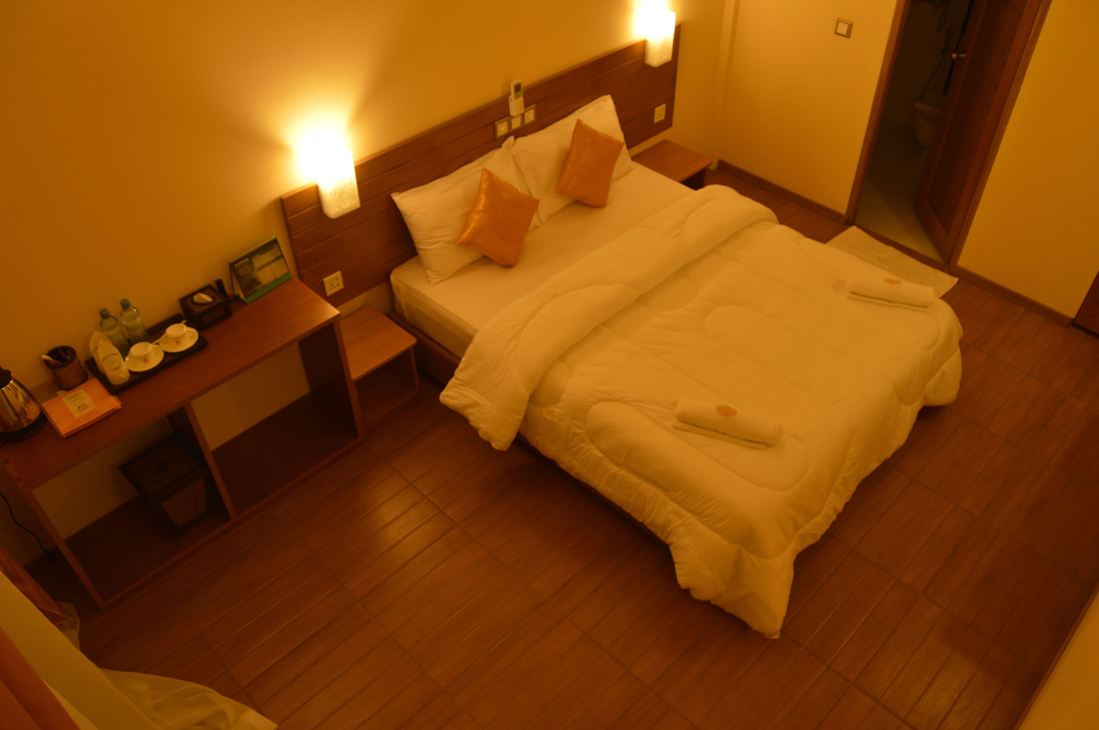 A hotel room with a large bed, two bedside tables, a nightstand, and a wooden floor.
