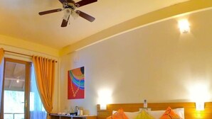 A hotel room with a bed, a desk with a chair, a ceiling fan, and a window with curtains. - Ocean Beach Inn - Maldives (Hangnaameedhoo)