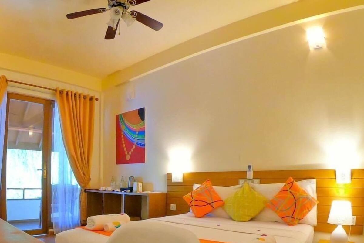 Una habitación de hotel con una cama, un escritorio con una silla, un ventilador de techo y una ventana con cortinas.