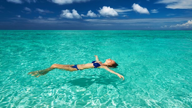 A person floating in clear turquoise water under a blue sky with clouds. - Ocean Beach Inn - Maldives (Hangnaameedhoo)