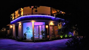 A multi-story hotel with a curved facade, illuminated by blue and purple lights. - Ocean Beach Inn - Maldives (Hangnaameedhoo)