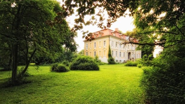A large, historic building with a red roof, surrounded by lush green grass and trees. - Schloss Stülpe (Nuthe-Urstromtal)