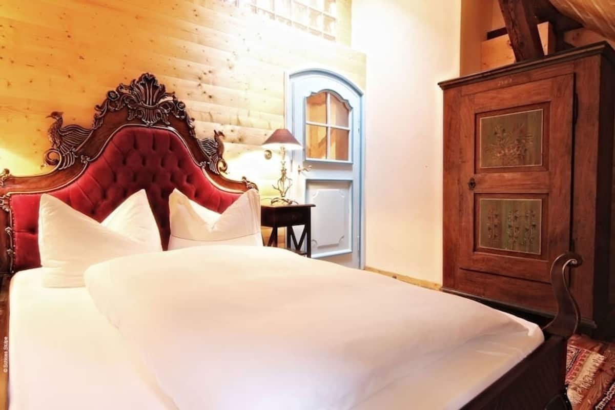A bed with a red headboard, white pillows, and a wooden headboard. There is a wooden cabinet with glass doors to the right.