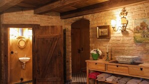 A rustic bathroom with a wooden door, a sink, a mirror, a wall-mounted light fixture, and a shelf with towels. - Schloss Stülpe (Nuthe-Urstromtal)