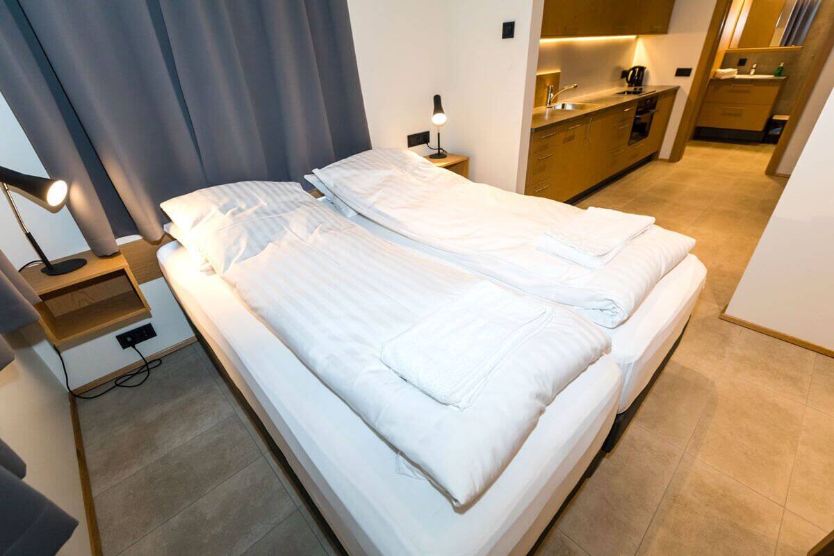 Een opgemaakt tweepersoonsbed met witte lakens, een bedlamp en een klein houten nachtkastje.