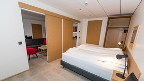 A modern hotel room with a bed, a desk, a chair, a wardrobe, and a bathroom visible through an open door. - Hrímland Apartments (Akureyri)