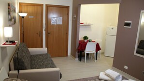 A hotel room with a sofa, a small table with a red tablecloth, a white chair, a refrigerator, and a door marked "privato". - Oasi Iblea (Ragusa)