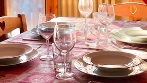 A dining table set with plates, glasses, and cutlery, with a view of a balcony and a window with curtains. - Case Vacanza Perron (Sauze d'Oulx)