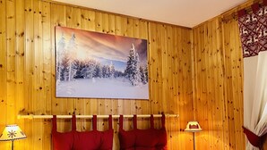 A cozy room with wooden panel walls, a bed with red bedding, and a winter-themed painting above the bed. - Case Vacanza Perron (Sauze d'Oulx)
