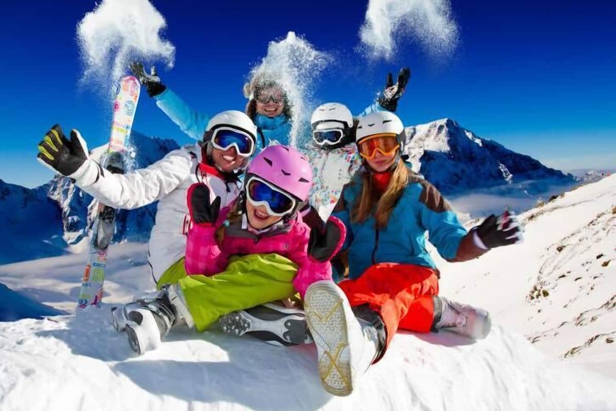 Um grupo de pessoas em uma montanha nevada com snowboards, usando capacetes e óculos de proteção.