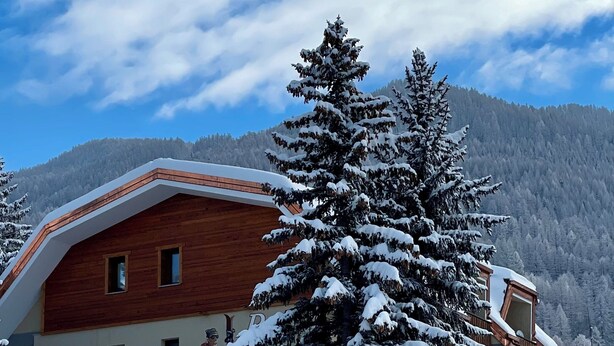 A wooden chalet with a sloped roof, surrounded by snow-covered trees and mountains. - Case Vacanza Perron (Sauze d'Oulx)