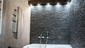 A modern bathroom with a freestanding bathtub, a mirror, and a stone-textured wall. - Art In B&B (Salerno)