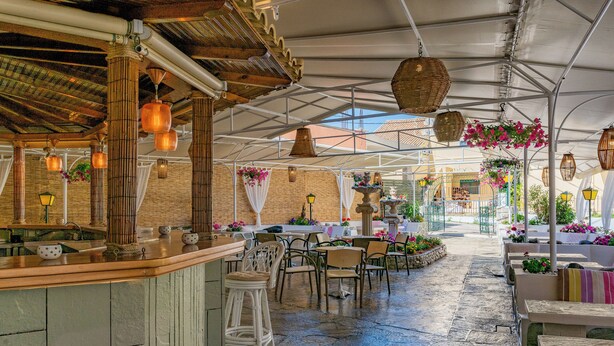An indoor patio area with stone flooring, wooden bar counter, and seating arrangements. - Hotel Sirena Beach (Corfu)