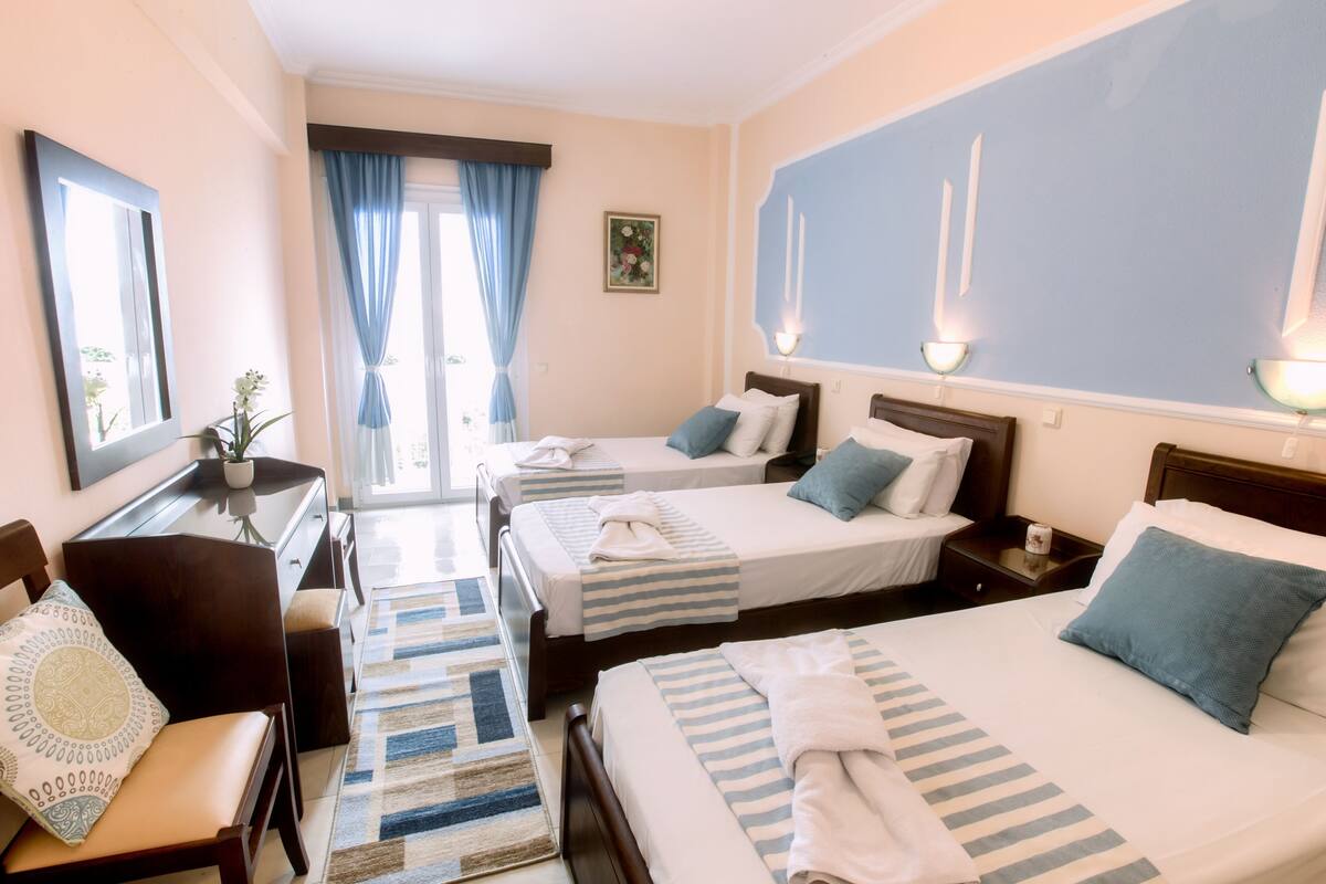 A hotel room with two beds, a desk, and a chair. There is a window with curtains, a painting on the wall, and a lamp on the nightstand.