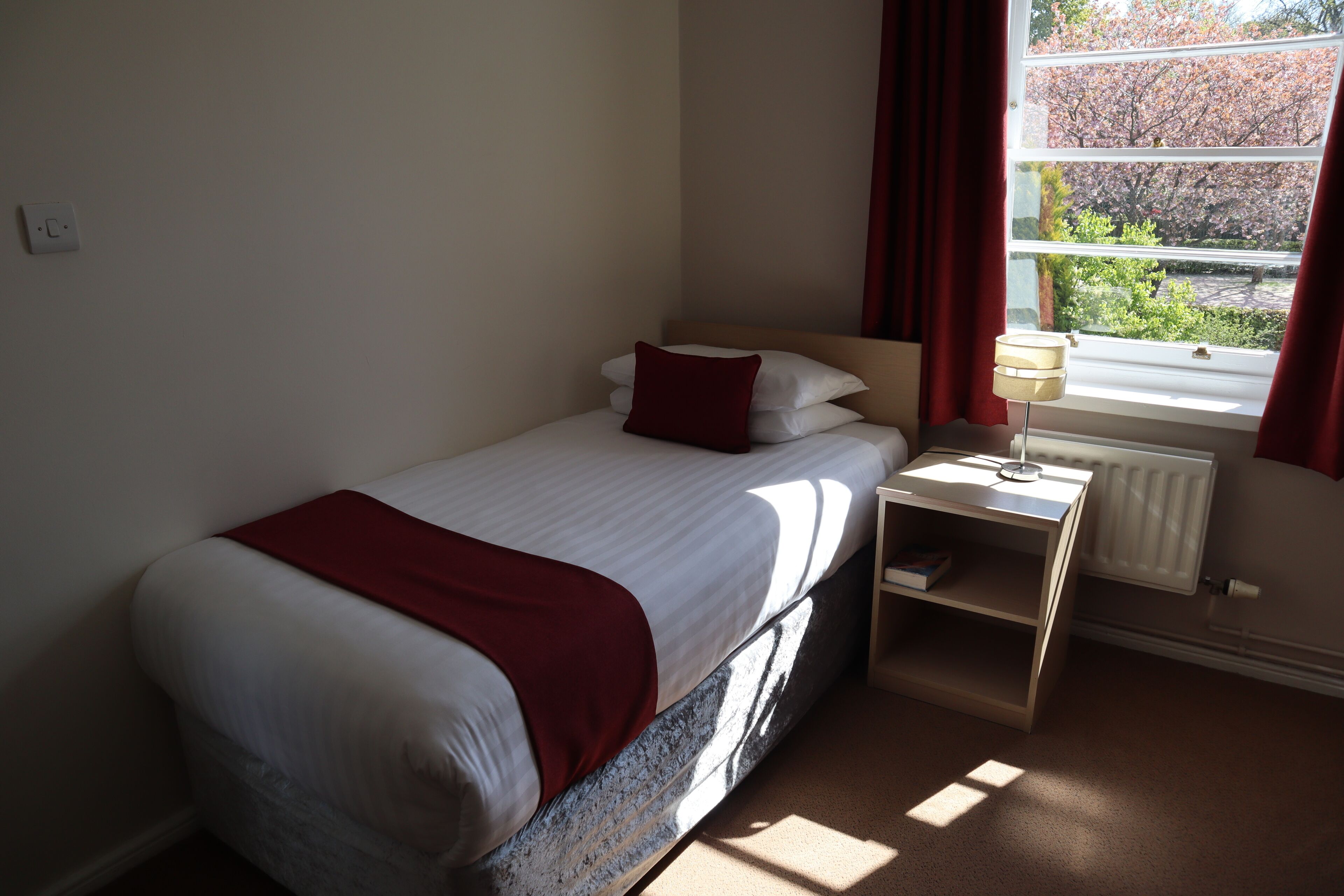 A bedroom with a bed, a nightstand, a lamp, and a window with curtains.