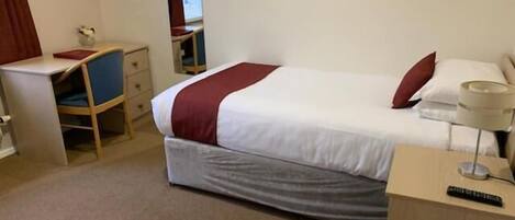 A hotel room with a bed, a desk, a chair, a lamp, and a remote control.