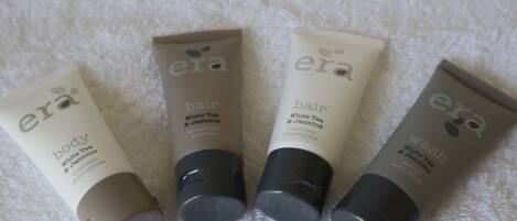 Cuatro botellas de crema corporal y acondicionador sobre una toalla blanca.
