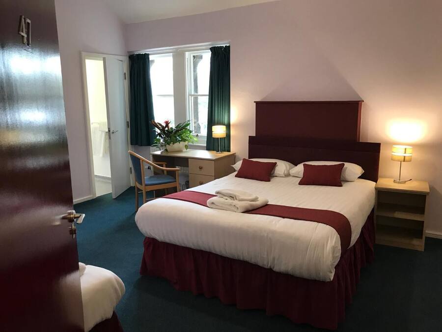 Habitación de hotel con cama, escritorio, silla y ventana con cortinas.