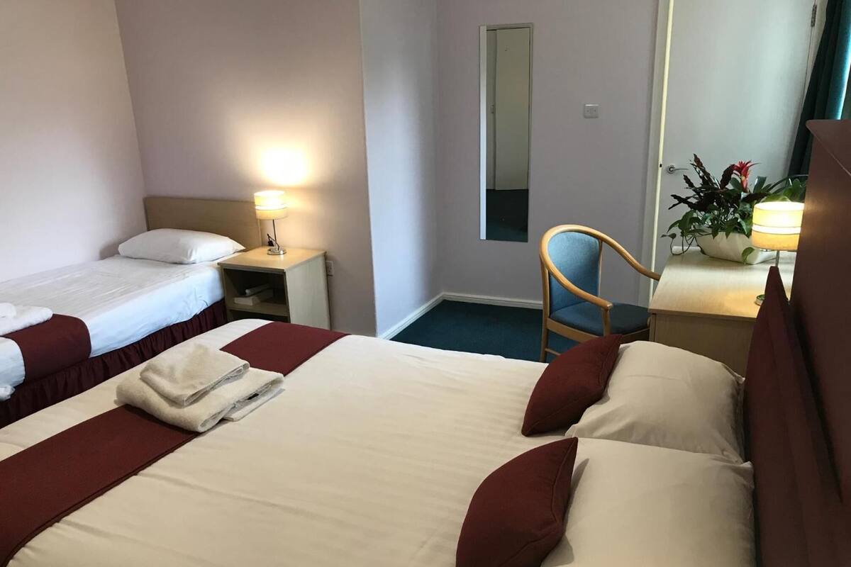 A hotel room with two beds, a chair, a desk, and a mirror.