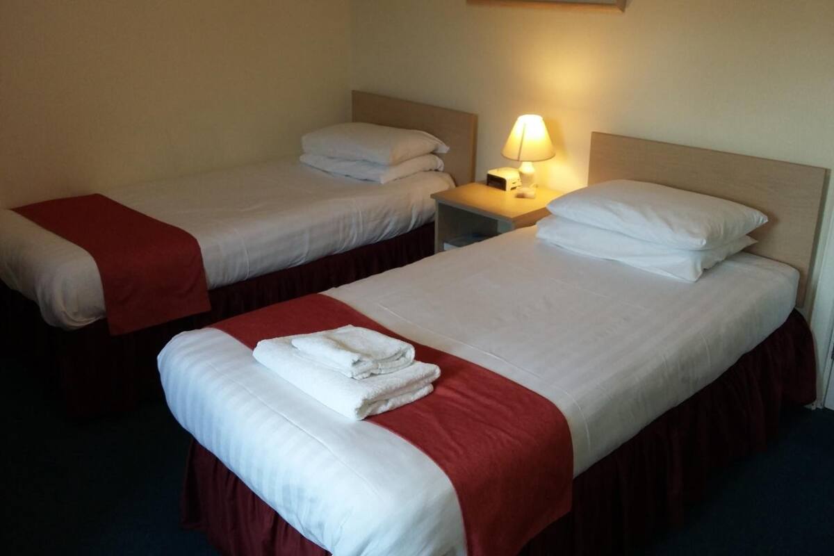 A hotel room with two single beds, each with a red bedspread and white linens. There is a nightstand with a lamp between the beds.