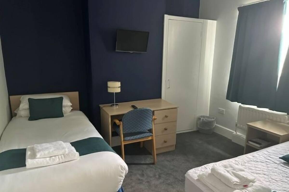 A hotel room with two beds, a desk, a chair, a TV, and a wardrobe.