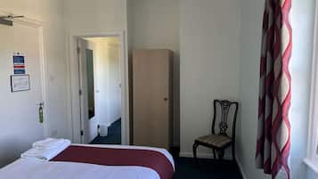 A hotel room with a bed, a chair, a wardrobe, and a window with curtains.