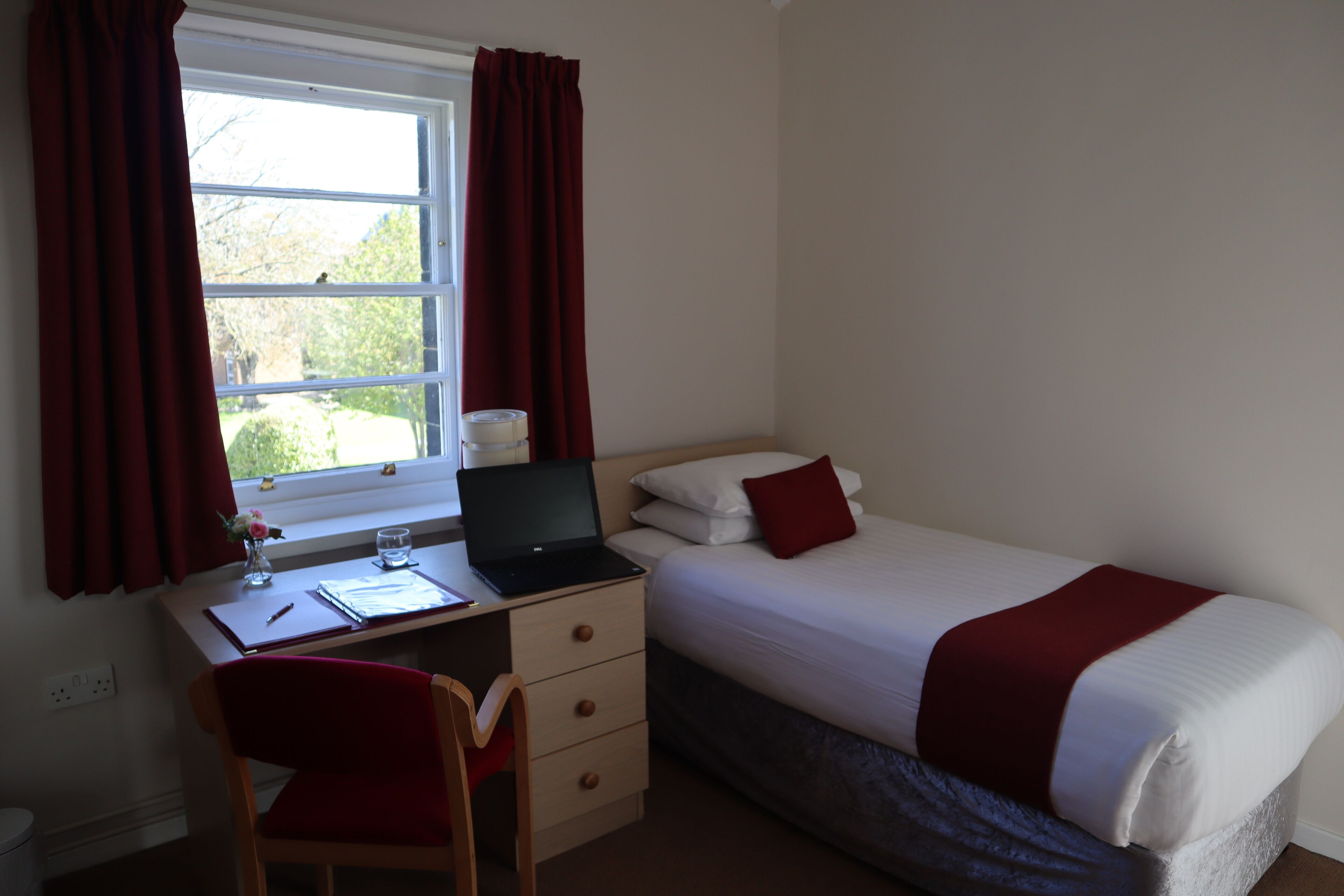 Ein Schlafzimmer mit einem Bett, einem Schreibtisch mit einem Laptop, einem Stuhl und einem Fenster mit Vorhängen.