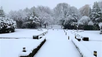 A snow-covered pathway leading through a park with trees and hedges.