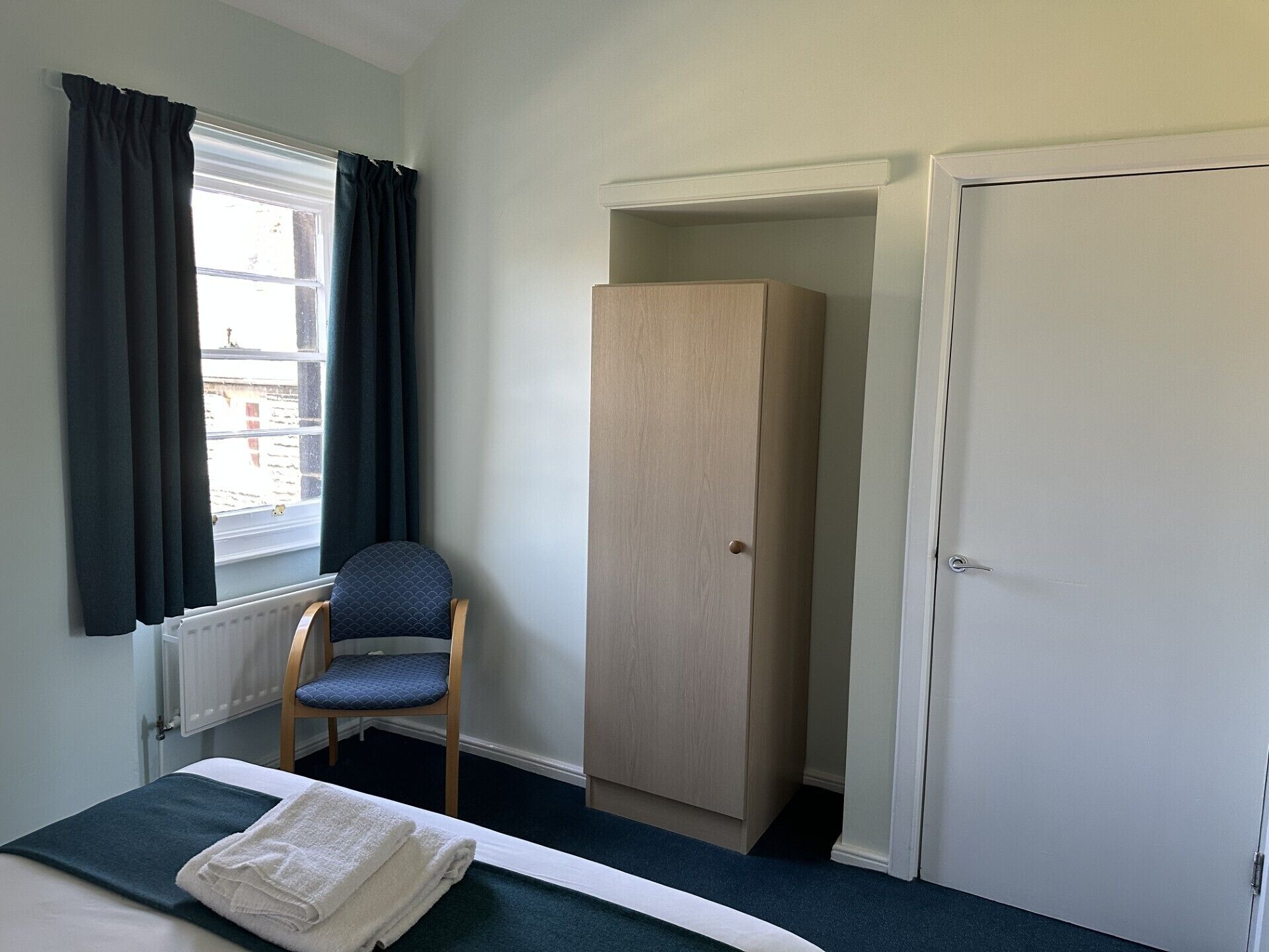 Une pièce comprenant un lit, une chaise, une armoire et une porte.