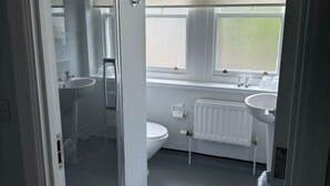 Un baño con cabina de ducha de vidrio, inodoro, lavamanos y ventana con persianas.