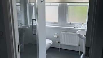 A bathroom with a glass shower enclosure, a toilet, a sink, and a window with blinds.