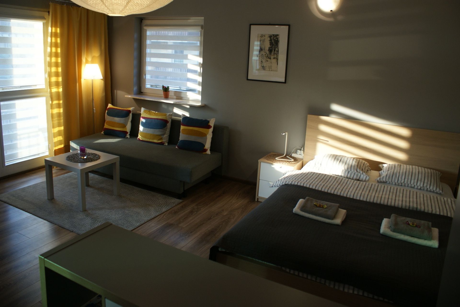 A modern hotel room with a sofa, a bed, a bedside table, and a lamp.