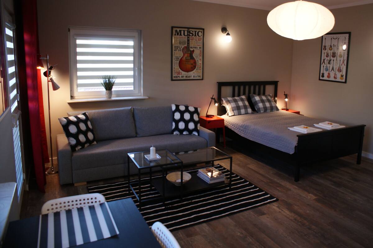 A modern bedroom with a bed, a sofa, a coffee table, and a window with blinds.