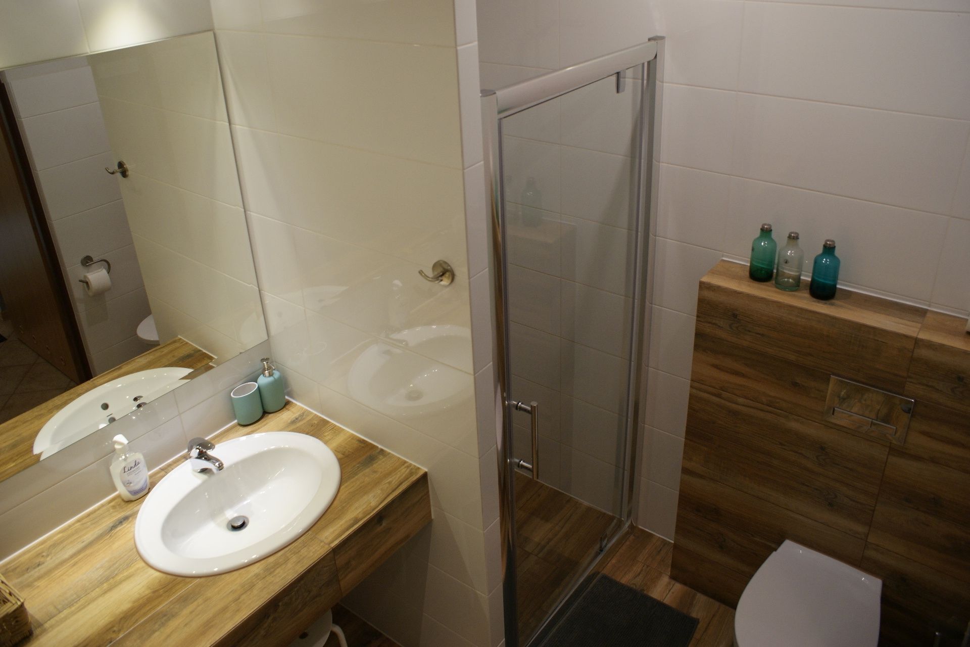 Une salle de bain moderne avec un meuble-lavabo en bois, une cabine de douche en verre et des toilettes.