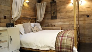 A wooden cabin-style bedroom with a bed, curtains, wall-mounted lights, and a bedside table.