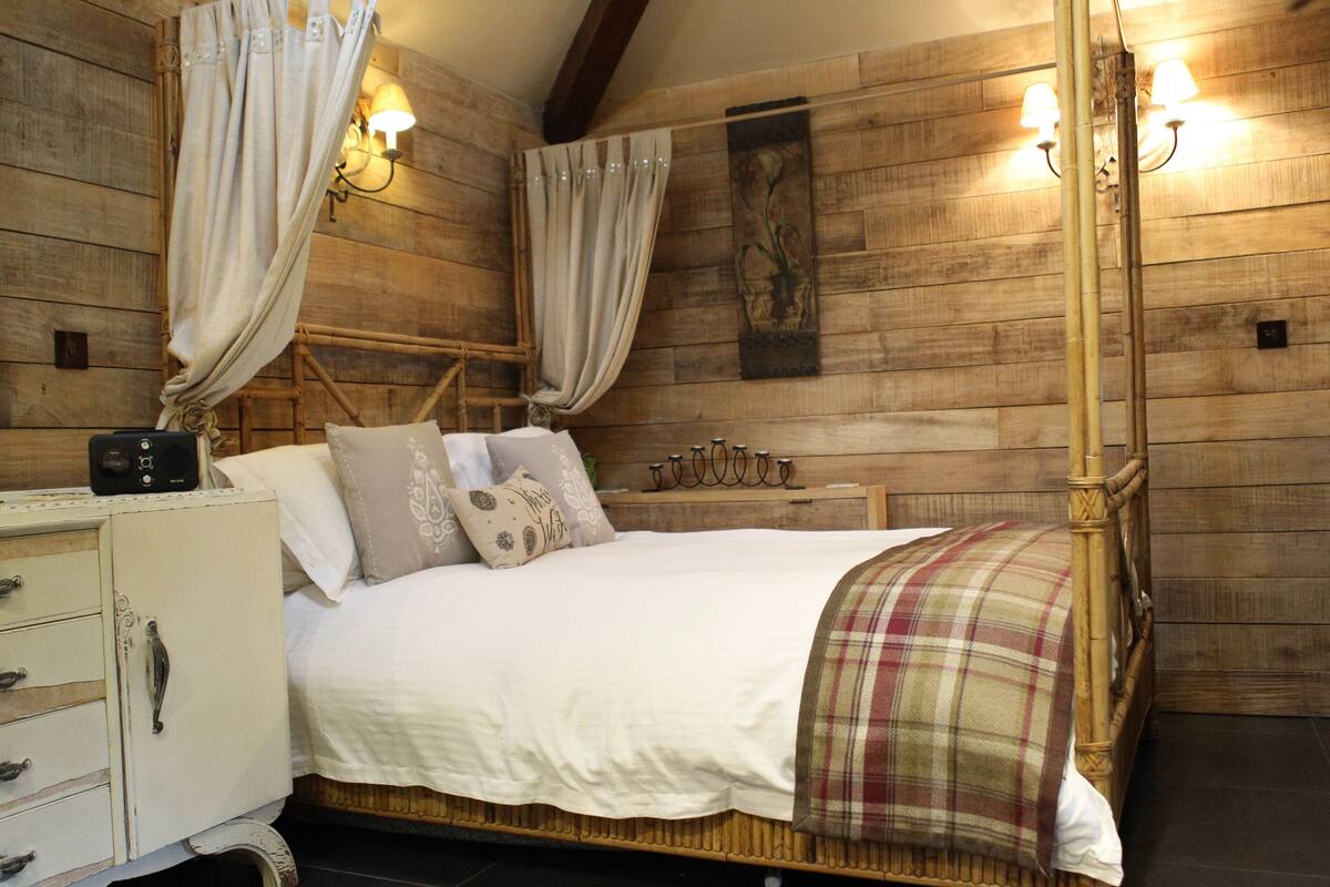 A wooden cabin-style bedroom with a bed, curtains, wall-mounted lights, and a bedside table.
