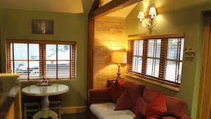 A cozy room with a round table, a red sofa, and a window with blinds.