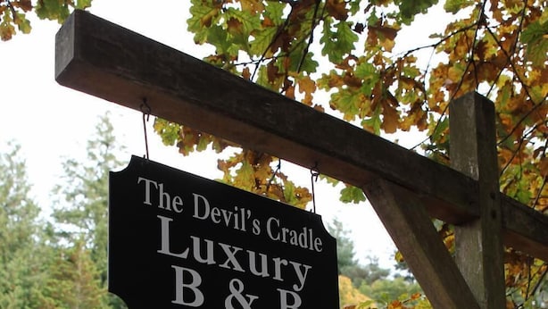 A sign for "The Devil's Cradle Luxury B&B" with a wooden gate and a house in the background.