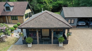 A small, single-story building with a pitched roof, a porch with a table and chairs, and a gravel driveway.