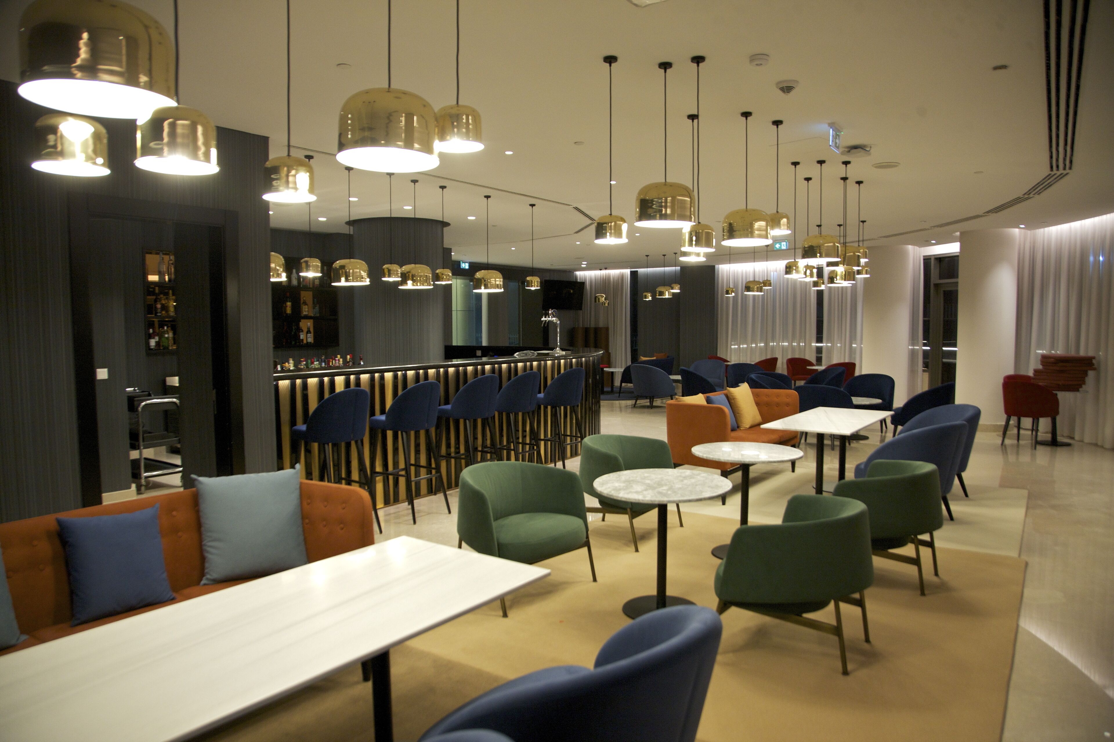 A modern restaurant with multiple seating areas, including tables and chairs, and a bar in the background.