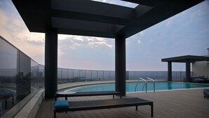 A rooftop pool area with a view of the city skyline, a lounge with a bench, and a covered seating area. - Hotel Continental Horizonte (Luanda)