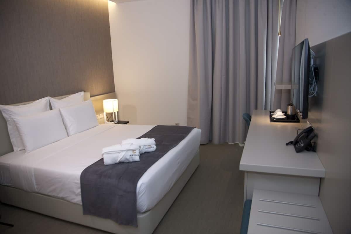 A hotel room with a bed, bedside table, lamp, and a flat-screen TV mounted on the wall.