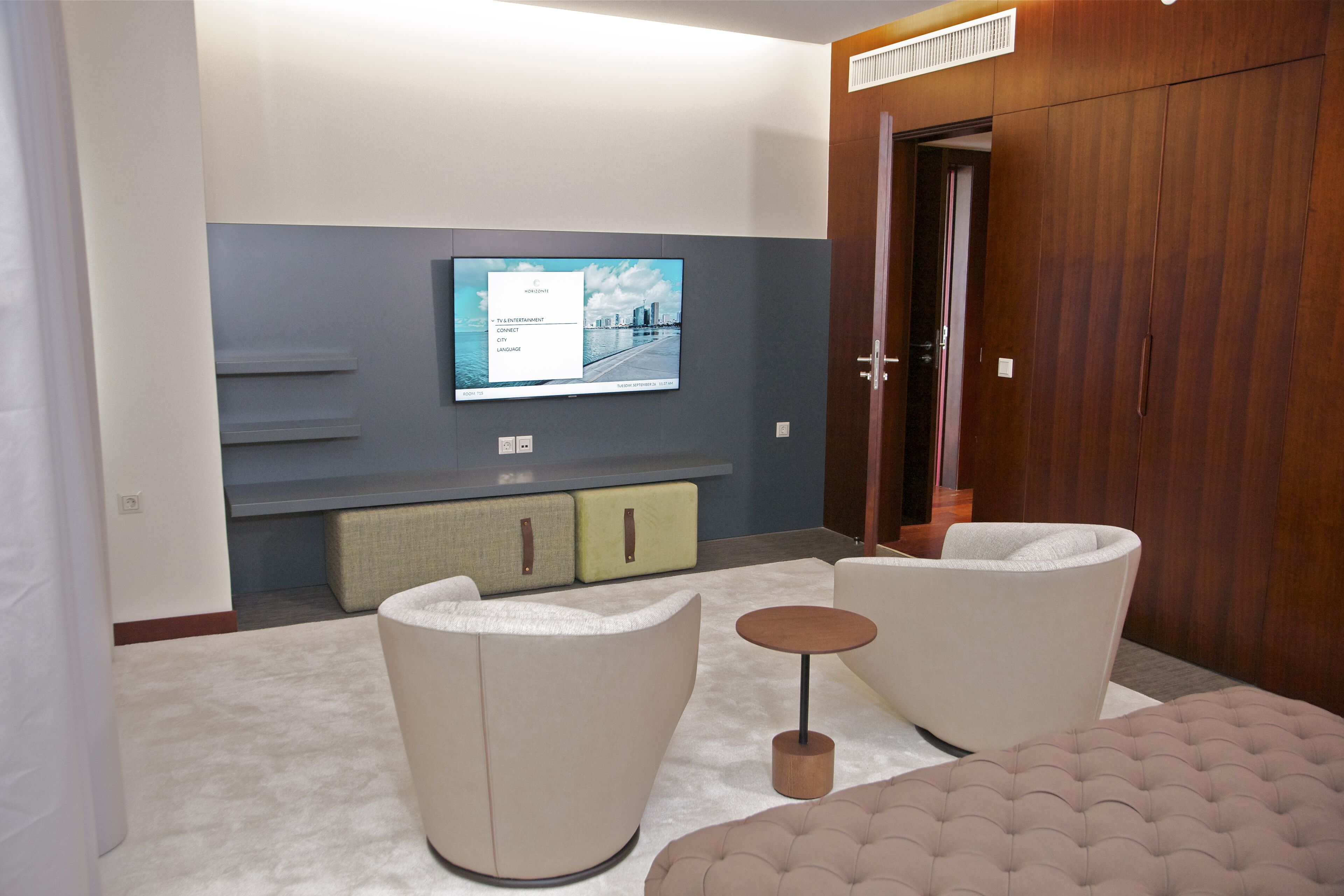 Una sala de estar moderna con una televisión de pantalla plana montada en la pared, un sofá, una mesa de centro redonda y unidades de almacenamiento empotradas.