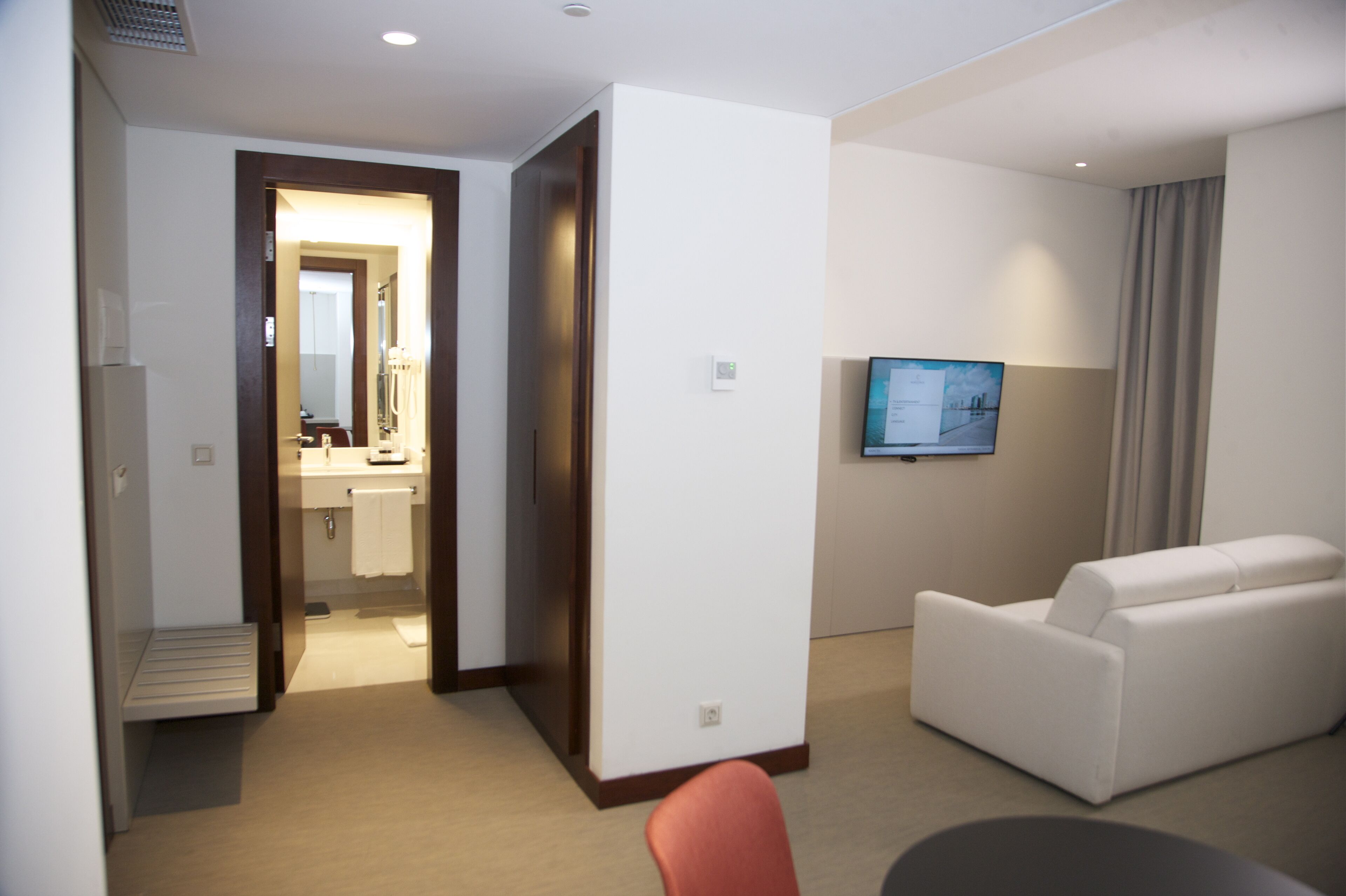 A hotel room with a sofa, a television, a bathroom with a sink and mirror, and a door leading to another room.